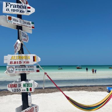 Panneaux directionnels sur une plage, avec des hamacs et un ciel bleu.