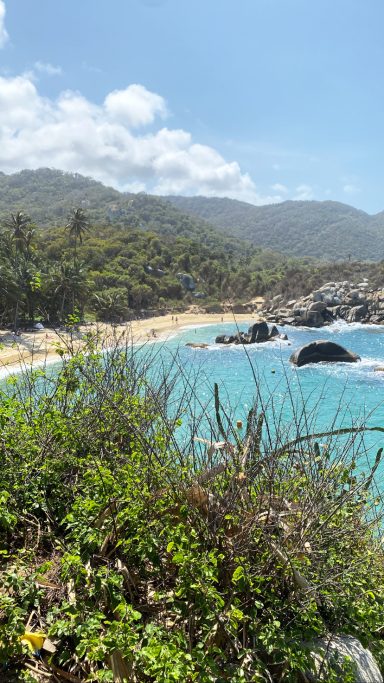 Plage entourée de végétation et de montagnes sous un ciel ensoleillé.