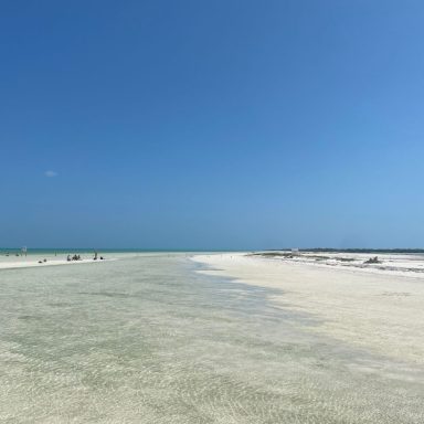 Plage vaste avec ciel bleu dégagé et mer en arrière-plan.