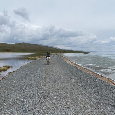 Un cavalier sur un chemin de gravier longeant une étendue d'eau sous un ciel nuageux.