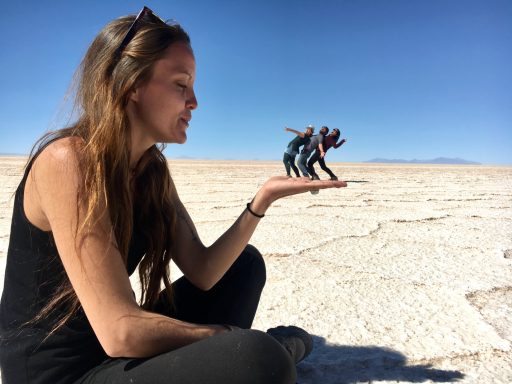 Une femme tenant de petites figurines dans sa paume, avec un paysage désertique en arrière-plan.