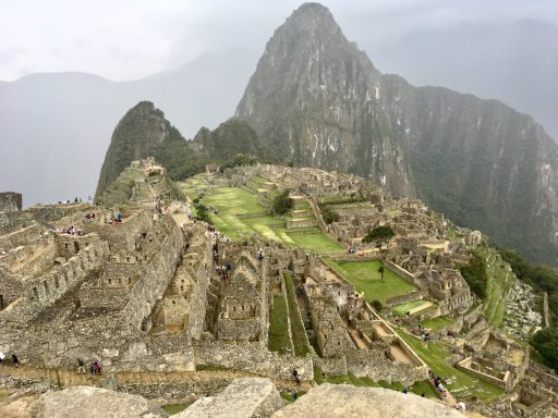 Ruines de Machu Picchu avec des montagnes en arrière-plan, sous un ciel nuageux.