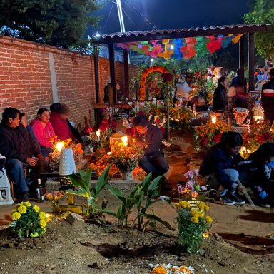 Célébration nocturne avec des personnes autour d'autels décorés de fleurs et bougies.