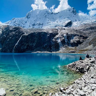 Lac turquoise aux reflets cristallins, entouré de montagnes enneigées sous un ciel bleu.