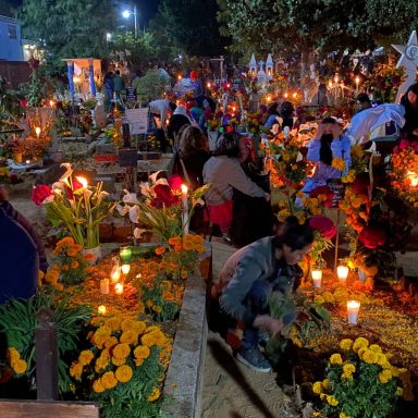 Cimetière illuminé par des bougies et des fleurs, rassemblant des personnes en deuil.