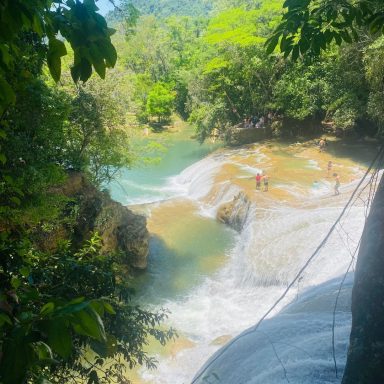 Chute d'eau entourée de verdure, avec des gens se baignant au bord.