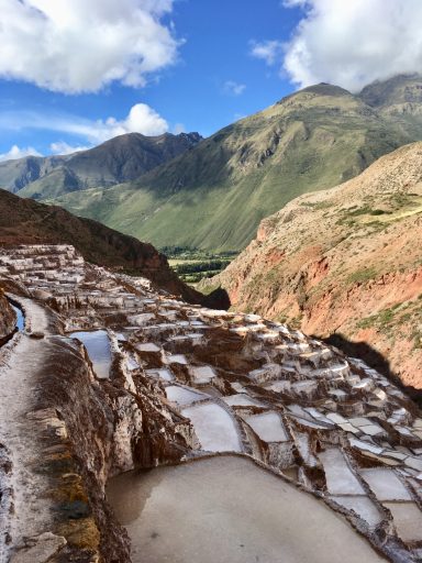 Terrasses de sel sur une montagne, avec des collines verdoyantes en arrière-plan.