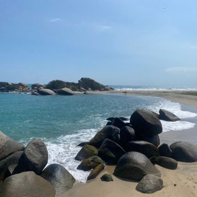 Plage tranquille avec des rochers et des vagues scintillantes sous un ciel clair.