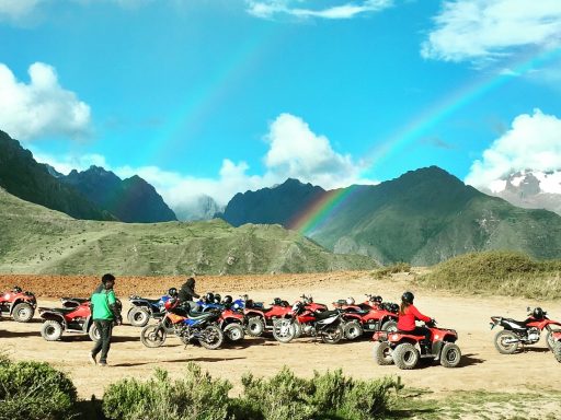 Des personnes en quad près d'une montagne, avec un arc-en-ciel dans le ciel clair.