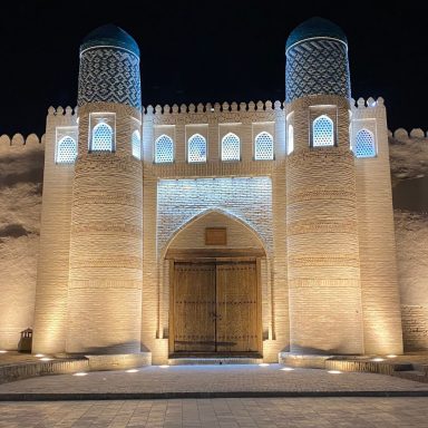 Grande porte en bois avec des tours décoratives, illuminée la nuit.