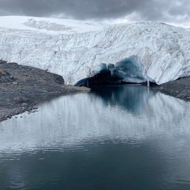 Glacier majestueux avec reflets dans un lac calme sous un ciel nuageux.