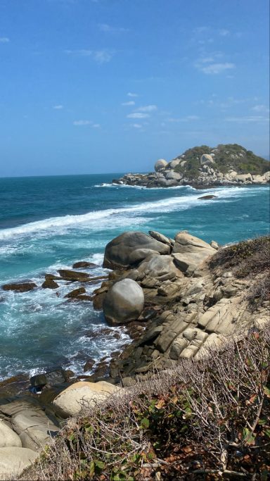 Vue sur une côte rocheuse avec des vagues et une colline à l'arrière-plan.