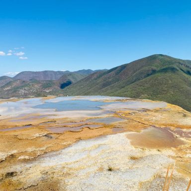 Lac couleur terre entouré de montagnes sous un ciel bleu clair.