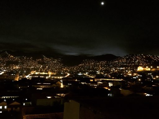 Vue nocturne de la ville avec des lumières scintillantes et des montagnes en arrière-plan.